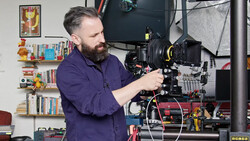 Cinematographer operating a large format film camera mounted on a rig in a studio setting.