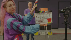Woman with pink hair holding a colorful rainbow pride flag during a film production shoot.