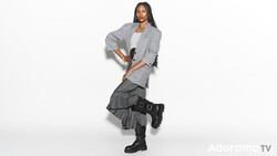 Woman in gray blazer and dark pleated skirt striking a dynamic pose against white background.