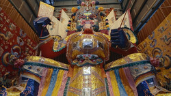 Large ornate golden statue with elaborate ceremonial dress and fierce expression displayed in a temple interior.