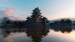 Japanese castle with tiered roofs reflected in still water at twilight.