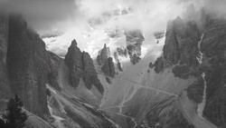 Dramatic black and white mountain landscape with towering rock formations and snow-capped peaks shrouded in clouds.