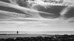 Solitary figure in wetsuit standing in shallow ocean water facing the horizon under dramatic sky.