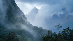 Misty mountain landscape with layered peaks shrouded in clouds and forested slopes.