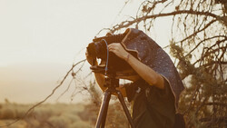 Photographer holding camera on tripod with umbrella in golden hour desert light.
