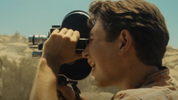 Cinematographer filming desert landscape with handheld movie camera in bright sunlight.