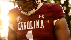 College football player in maroon uniform with Riddell helmet and Under Armour gear, photographed in golden hour sunlight.