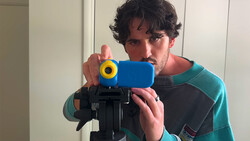 Photographer holding a smartphone mounted on a tripod with a blue phone holder and yellow counterweight.