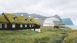 Traditional turf-roofed house with black walls and moss-covered roof overlooking coastal cliffs and mountains.