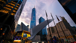 Modern skyscraper with blue glass facade towers above surrounding buildings in urban downtown district at dusk.