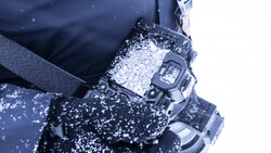Digital watch covered in snow and ice, worn on a wrist with winter gloves and dark jacket.
