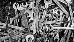 Overhead black and white arrangement of various wrenches and hand tools scattered densely across the frame.