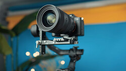 Camera lens mounted on a gimbal stabilizer against a blue and yellow blurred background.