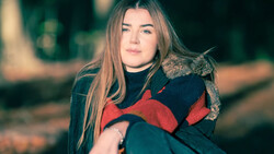 Woman with long brown hair holding a tabby cat while wearing a dark sweater with red accents.