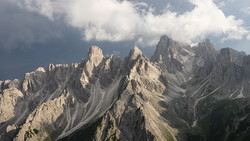 Dramatic limestone peaks of the Dolomites with layered ridges under cloudy sky.