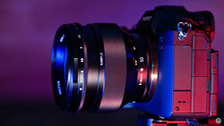 Red mirrorless camera with mounted prime lens against purple background with blue accent lighting.