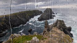 Rocky coastline with turquoise water viewed through rain-covered glass.