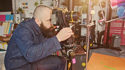 Filmmaker operating a large format movie camera mounted on a tripod in a studio workspace.