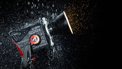 Overhead view of a camera or electronic device with water droplets and sparks creating dynamic motion effect against dark background.
