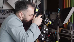 Bearded photographer looking through large format camera viewfinder in studio setting.