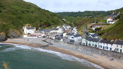 Coastal village nestled between green hills and a sandy beach with breaking waves.