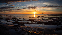 Golden sunset over rocky coastline with calm water reflecting warm light across the horizon.
