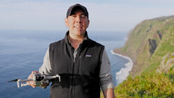 Man holding a drone while standing on a coastal cliff overlooking the ocean.