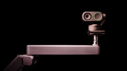 Rose gold mirrorless camera mounted on an articulating arm against a black background.