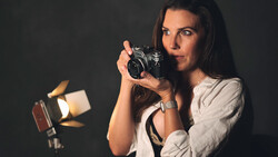 Female photographer holding a vintage SLR camera, illuminated by studio lighting against a dark background.