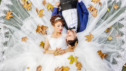 Bride and groom lying on ground surrounded by autumn leaves and tulle fabric.