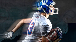 Football player in blue and white uniform holding ball with motion blur effect.