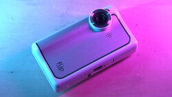 Compact camera device with prominent lens on vibrant neon blue and pink gradient background.