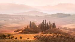 Tuscan villa surrounded by cypress trees on a hilltop in misty golden landscape.