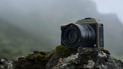 Medium format camera with telephoto lens positioned on a moss-covered rock in fog.