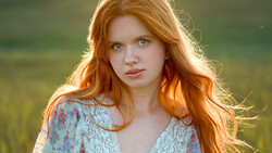 Portrait of a young woman with long red hair wearing a floral lace top, backlit by golden hour sunlight.