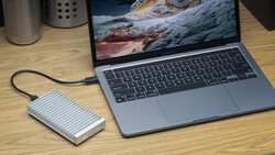 MacBook Pro laptop connected to external portable SSD via USB-C cable on wooden desk.