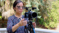 Cinematographer operating a cinema camera mounted on a tripod with follow focus gear in an outdoor garden setting.