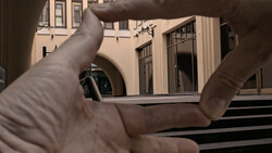 Hands framing a courtyard view through a window opening, with classical architecture visible beyond.