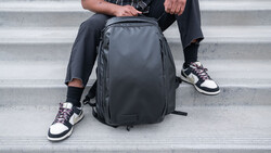 Person sitting on concrete steps holding a dark gray backpack with organizational compartments.