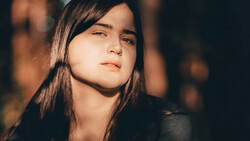 Young woman with long dark hair gazing upward in warm golden light against a dark background.