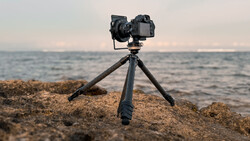 Professional camera mounted on tripod positioned on rocky beach overlooking calm ocean at sunset.