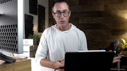 Man wearing glasses working at laptop in modern office space with ambient lighting.
