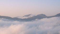 Mountain peaks rising above a sea of clouds at dawn, with soft purple and pink light illuminating the misty landscape.