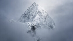 Snow-covered mountain peak emerging through dense clouds and mist.