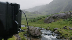 Camera mounted on tripod overlooking a misty mountain valley with a stream and green meadows.
