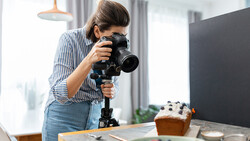Photographer using a telephoto lens mounted on a tripod while shooting a styled food scene indoors.
