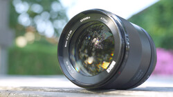 Black prime lens positioned on wooden surface with blurred garden and flowering plants in background.