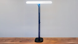 Modern desk lamp with tall dark blue-black stand and white LED panel on wooden surface.