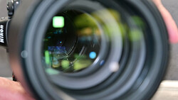 Close-up view through a Nikon lens barrel showing internal glass elements and optical coatings with green and blue reflections.