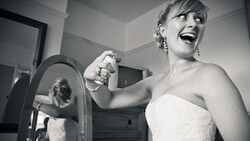 Bride in strapless wedding dress smiling while holding handheld mirror in black and white portrait.